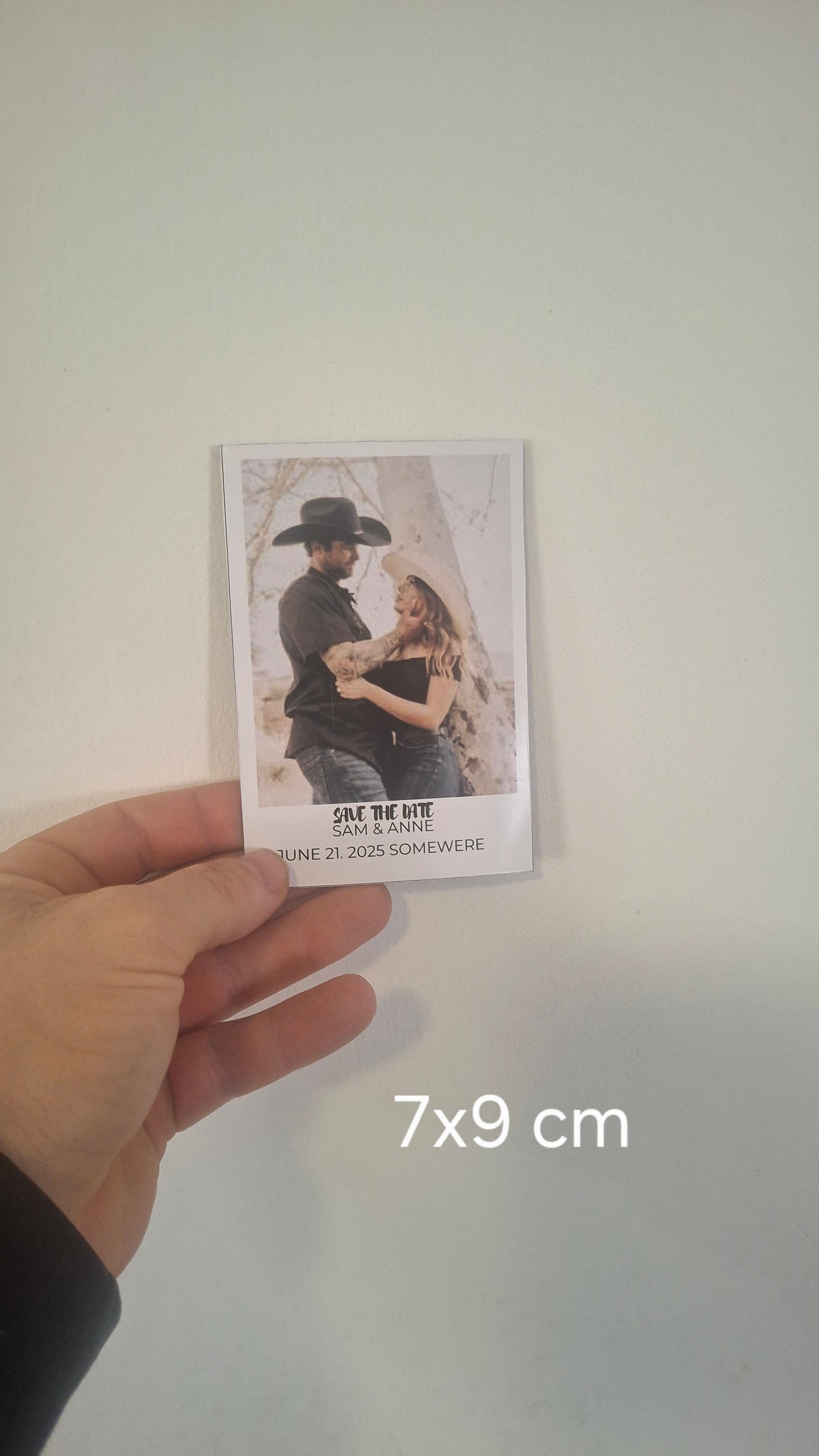 Hand holding a small card with a printed image of a couple, size 7x9 cm, on a plain background.